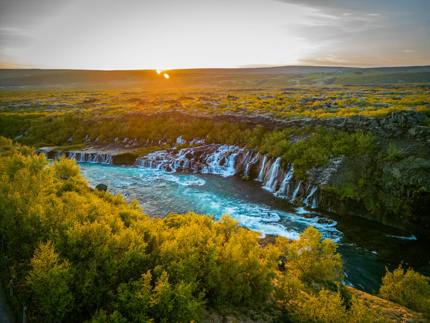 River cascading over waterfalls near colorful bushes and dark rocks.