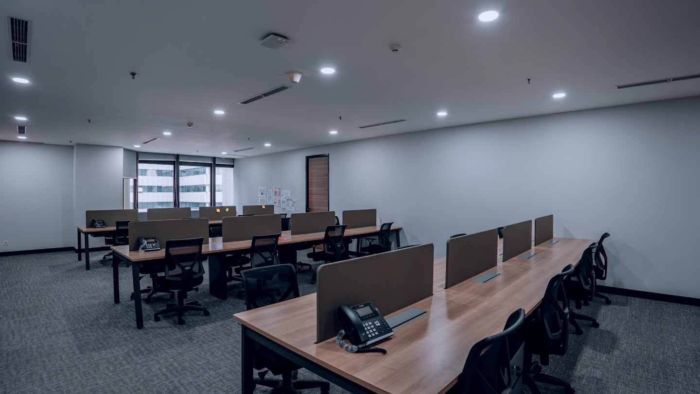 Empty modern office with rows of desks and black chairs.